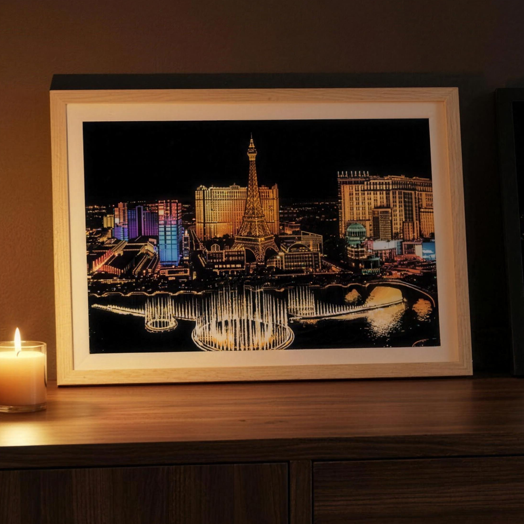 The Scratchlight Frame in natural wood holding a finished Las Vegas scratch art card, candle beside it