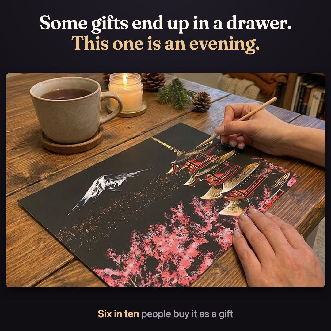 Hands scratching the Mount Fuji card at a wooden table, with a cup of tea and a candle. Some gifts end up in a drawer. This one is an evening. Six in ten people buy it as a gift.